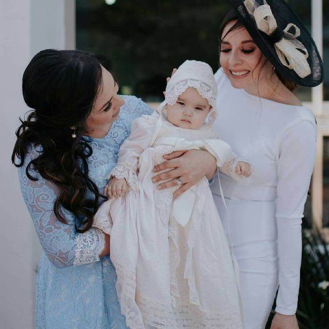 Carmen Varona Moda Infantil mujeres con traje de bautizo sujetan bebe con capucha bordada